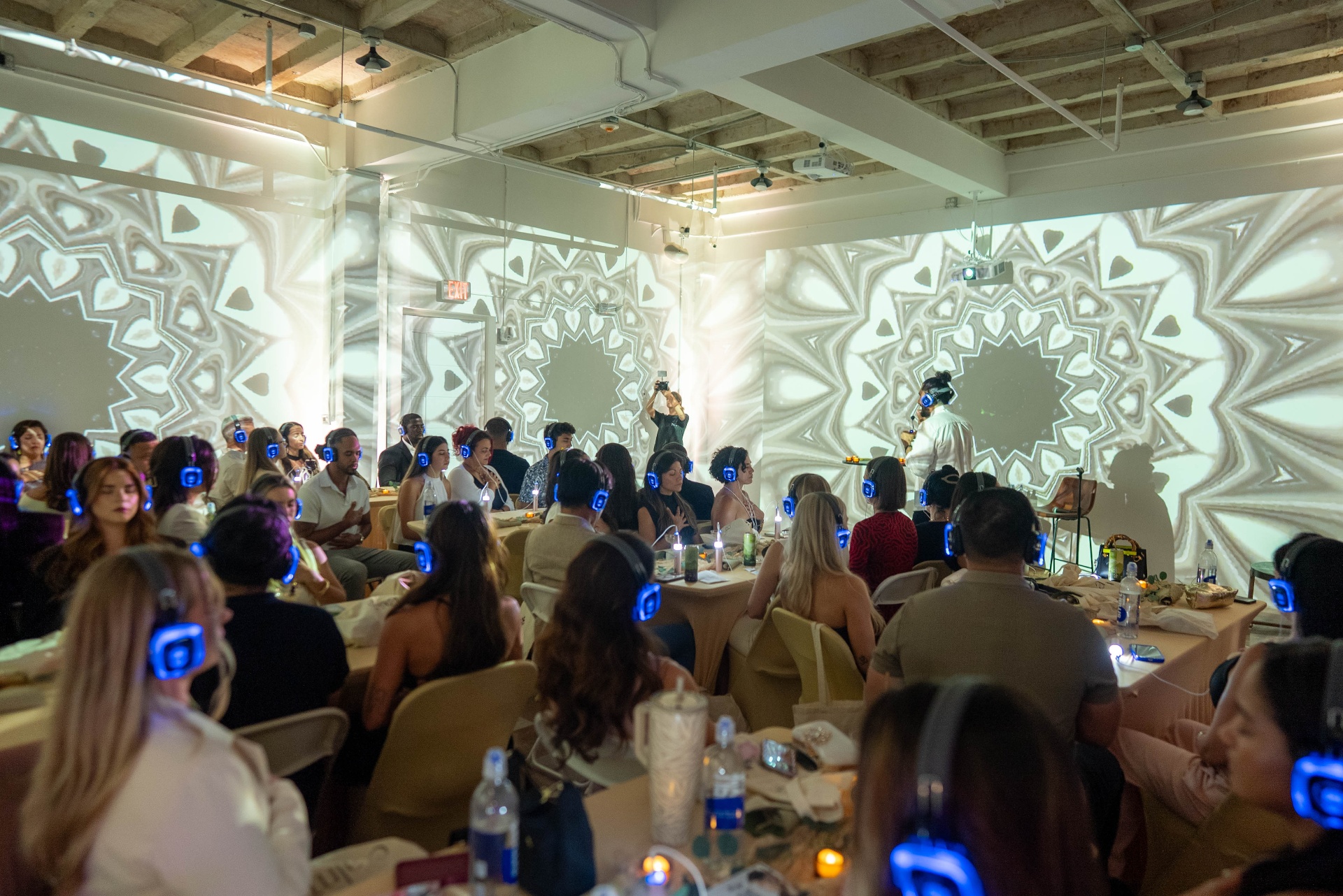 Members in a sound meditation session at CALMA, wireless headphones lit blue, kaleidoscope light projected on the walls